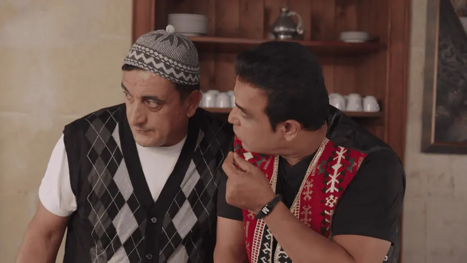 6. bölümden sahne: takkeli yaşlı bir adam ile geleneksel yelekli adam sohbet ediyor